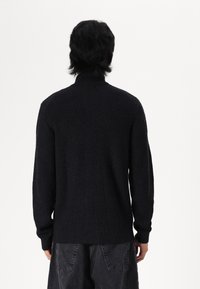 Svart ribbad tröja med hög krage, långa ärmar och en texturerad yta. Designen har en figursydd silhuett vid midjan.