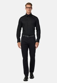Must have pikkade varrukatega must nööbitav särk, millega on sobitatud mustad püksid ja mustad elegantsed kingad. Materjal tundub sile; sisaldab vööd. Ahn ikka riietus.