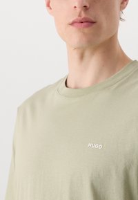 Lysegrøn t-shirt med rund halsudskæring, korte ærmer og et lille hvidt logo, der står "HUGO" på venstre side af brystet.