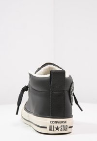 Czarne skórzane wysokie sneakersy z białym sztucznym futrem wewnątrz. Posiadają czarne sznurówki, tylną pętlę oraz gumową podeszwę z logotypem "Converse All Star".