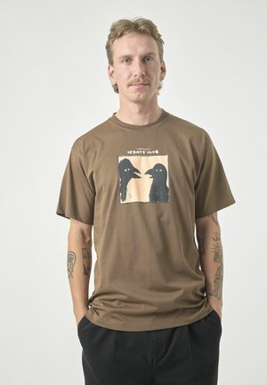 Brown cotton t-shirt featuring a graphic print of two black birds on a cream background, with short sleeves and a round neckline.