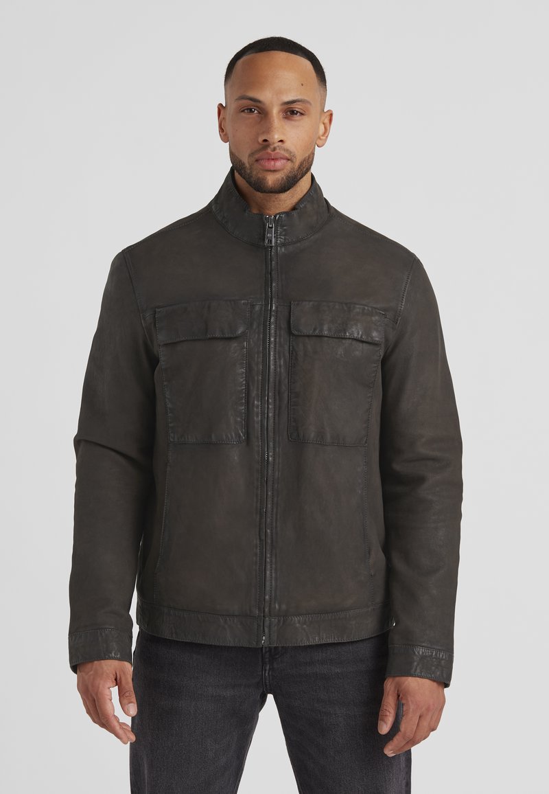 Dunkle Lederjacke mit hohem Kragen, Frontreißverschluss und zwei Brusttaschen. Glatte Oberfläche und taillierte Passform, kombiniert mit dunklen Jeans.
