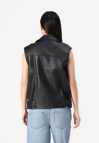 Črna usnjena brezrokavna jakna z izrezanim ovratnikom, dvema stranskima žepoma in nastavljivimi trakovi na pasu, z strukturo na površini.