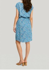 Robe bleu clair à manches courtes, taille élastique et motif floral rose et vert. Tissu lisse et coupe au genou. Sandales à talons carrés marron.