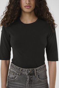 Melna īsroku krekls ar apaļu kakla izgriezumu, kombinēts ar augsta vidukļa, izbalināti pelēkām džinsu biksēm, kurās ir pogas aizdare un priekšējās kabatas.