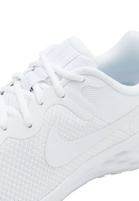 Shoe sportiv alb cu un upper din plasă, accente netede și logo-ul distinctiv. Sireturi plate, cu un călcâi căptușit și o talpă texturată.