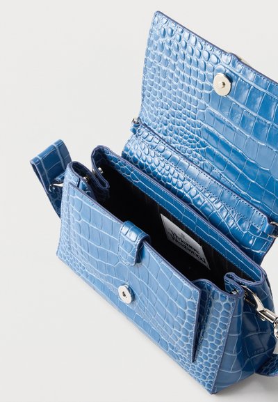 Μπλε τσάντα χιαστί από συνθετικό δέρμα κροκό με κλείσιμο με μαγνητικό καπάκι, ανοιχτή για να αποκαλύψει το μαύρο εσωτερικό και μια ετικέτα μέσα.