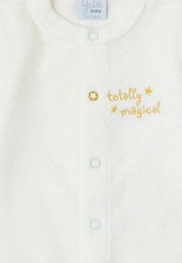 Conjunto de ropa para bebé de tela blanca con un patrón texturizado, que incluye un botón en forma de estrella amarilla y texto bordado "totalmente mágico" en amarillo.
