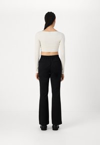 Pantalons noirs évasés avec une taille élastique et des poches arrière, associés à un haut ajusté à manches longues crème, vus de dos.