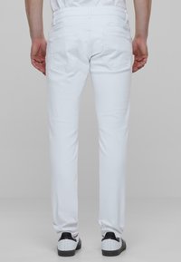Vaqueros de mezclilla blanca con corte ajustado, bolsillos traseros estándar y una textura suave, combinados con zapatillas blancas y negras.
