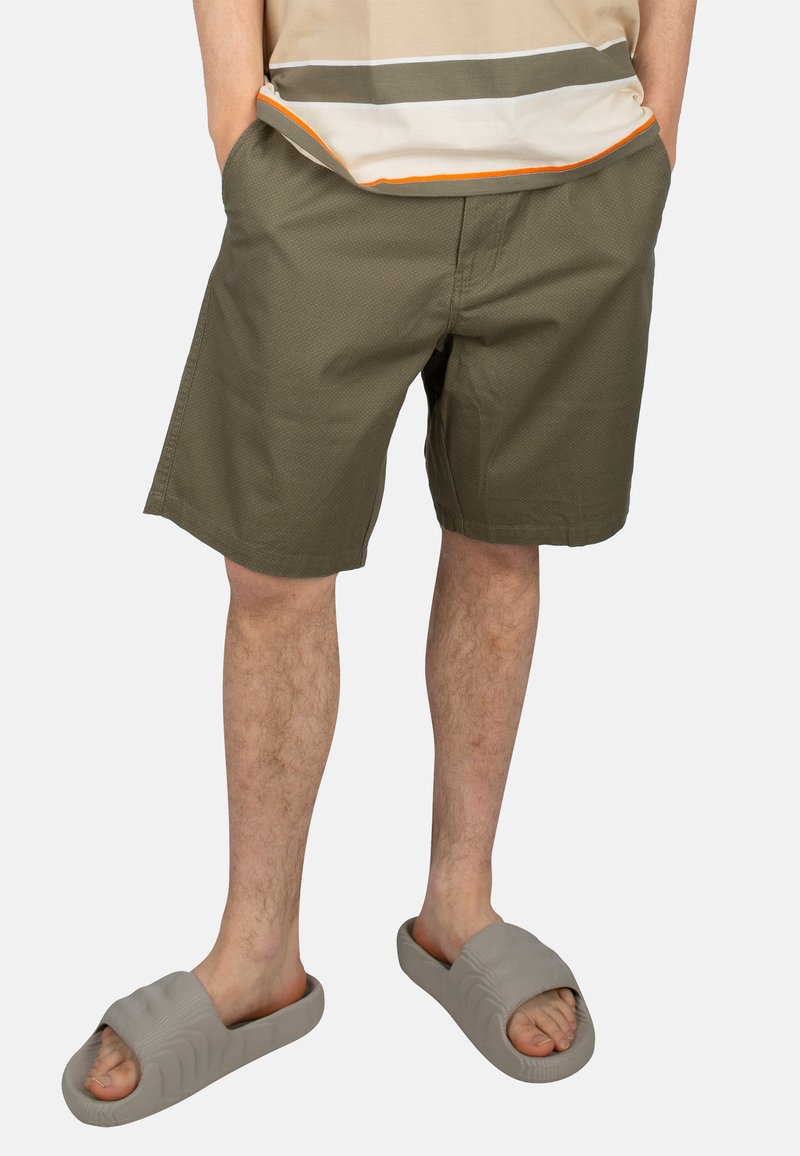 Khaki shorts made of textured fabric, featuring side pockets and a comfortable fit. Worn with grey slip-on sandals.