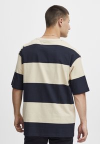 Pruhované oversized tričko v béžové a námořnické barvě, s krátkým rukávem, volným střihem a kulatým výstřihem. Lehce bavlněný materiál.