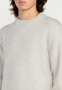 Lys grå ullgenser med høy, ribbet halslinning og lange ermer. Teksturen virker myk og litt fuzzy. Minimalistisk design.