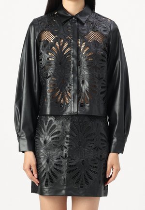 Femme portant une chemise en cuir noire et une jupe avec de grands motifs floraux découpés laissant apparaître la peau en dessous.
