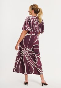 Lilla blomster maxikjole med korte ærmer, der har en smocket ryg, hvid blomsterprint og en luftig, let stofstruktur.