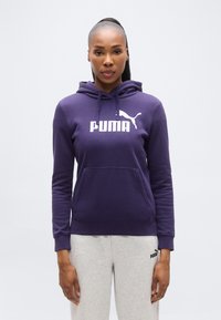 Μωβ φούτερ με κουκούλα και τσέπη καγκουρό, με λευκό λογότυπο και έμβλημα "PUMA". Συνδυάζεται με γκρι φόρμα. Το ύφασμα φαίνεται απαλό και άνετο.