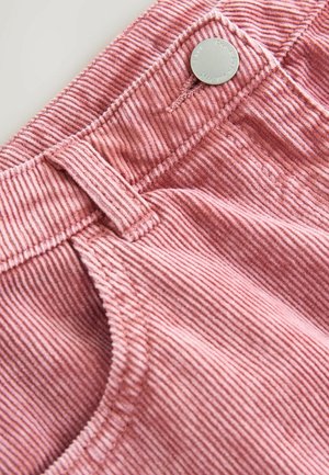 Tissu en velours côtelé rose avec des rayures verticales. Comprend un bouton en métal et une passante de ceinture à la taille. La texture est douce et côtelée.