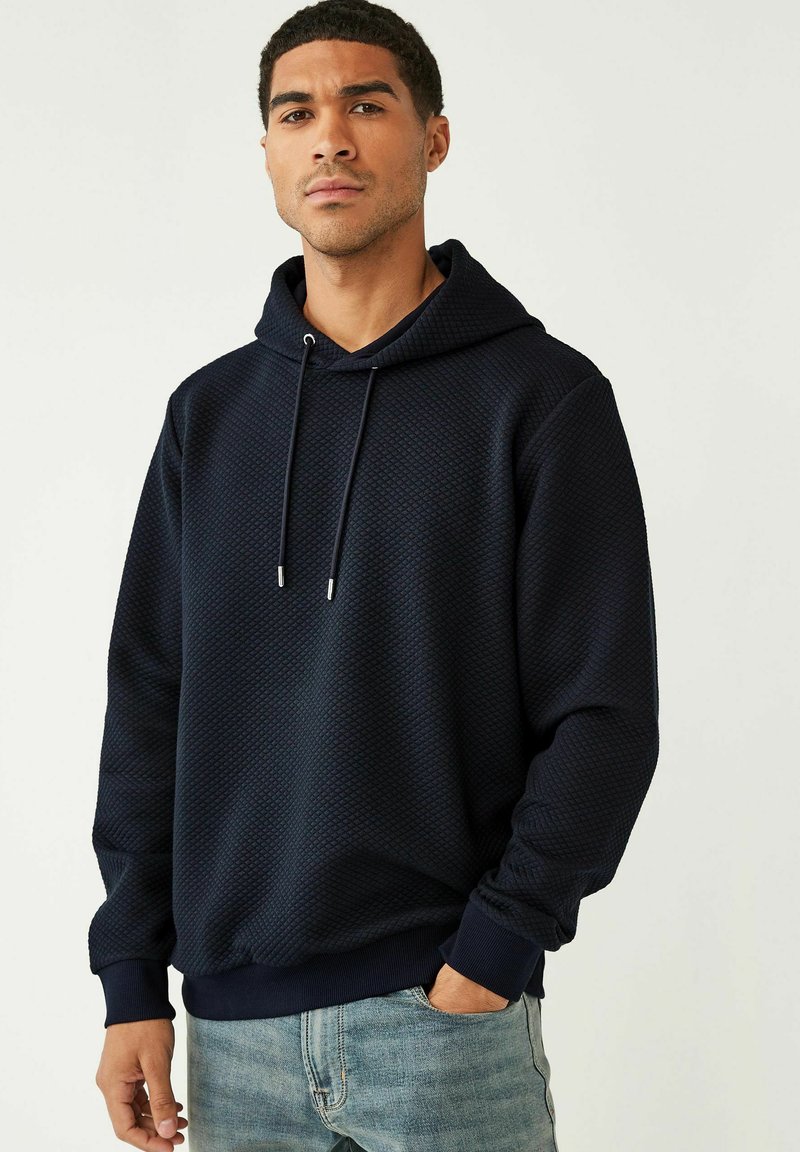 Marineblauwe hoodie gemaakt van gestructureerde stof met een ruitpatroon. Voorzien van trekkoorden en geribbelde manchetten voor een snug fit.