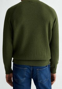 Pull vert foncé en tricot avec poignets et ourlet côtelés, doté d'un dos texturé et de manches raglan. Associé à un jean en denim bleu.