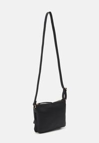 Sac à bandoulière en cuir noir avec une forme mince, fermeture zippée en haut, et une seule sangle avec des accents en métal doré. Texture lisse et design minimaliste.