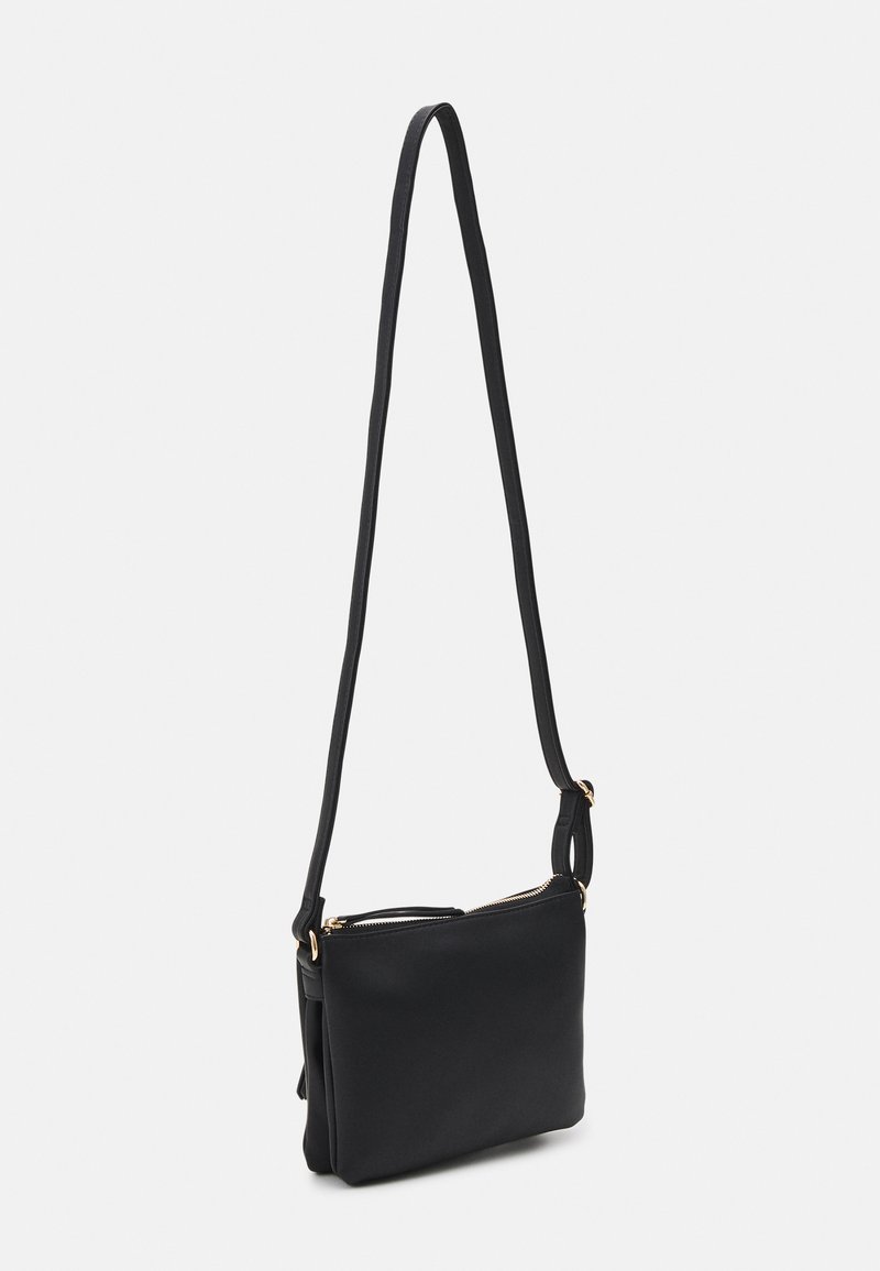 Bolso cruzado de cuero negro con una forma delgada, cierre superior con cremallera y una sola correa con acentos dorados. Textura suave y diseño minimalista.