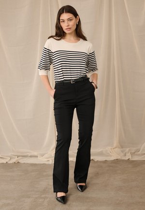 Striped oversized T-shirt in cream and navy paired with tailored black trousers and black pointed-toe heels. Simple belt at the waist.