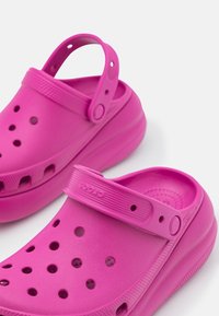 Jasně růžové d�řeváky vyrobené ze syntetického materiálu, s vyvýšeným, strukturovaným páskem, ventilačními otvory a zaobleným tvarem.