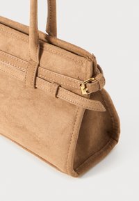 Sac à main en suède beige avec deux poignées courtes, de forme rectangulaire, détail de couture, et une boucle en métal doré sur une sangle.