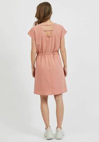 Růžové šaty s krátkými rukávy, staženým pasem a výstřihem do V na zádech s vodorovnými pásky. Vyrobené z hladké látky, sahají po kolena, minimalistický design.