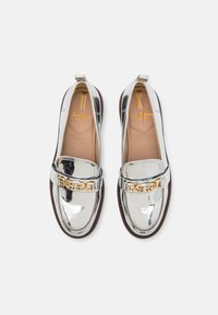 Sølv patent lær loafers med en chunky gullkjede aksent over forsiden. Polstret såle og en teksturert brun såle.