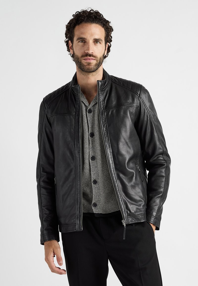 Svart läderjacka med ståkrage och vadderade axeldetaljer, kombinerad med en randig henleytröja och mörka byxor.