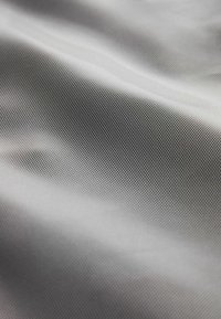Maschenstoff mit feinem Gittermuster in verschiedenen Grautönen, der eine glatte, leicht glänzende Textur aufweist. Das Licht spiegelt subtil wider und erzeugt Tiefe.