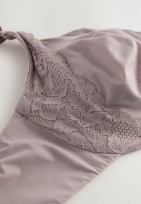 Soutien-gorge en tissu mauve doux avec une garniture en dentelle florale détaillée en haut, texture lisse et bretelles réglables.