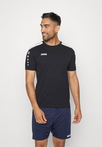 Zwart sport T-shirt met witte zijkanten, korte mouwen en het "JAKO" logo op de borst. Bevat ronde accenten op de schouder.