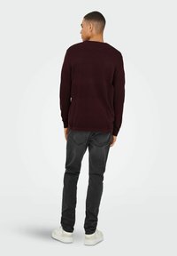 Bordeaux gebreide trui met een textuurpatroon, gecombineerd met donkergrijze jeans en witte sneakers. Achteraanzicht, minimale details zichtbaar.