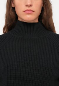 Schwarzer gerippter Rollkragenpullover mit einem strukturierten Strickdesign, hohem Kragen und Raglanärmeln, ideal zum Schichten.