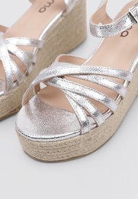 Sandalias de plataforma metálicas plateadas con tiras entrelazadas, plantilla de yute trenzado y superficie superior texturizada. Suela de goma para mayor agarre.