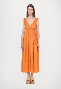 Orange, veckad maxiklänning med djup V-ringning och omslagdesign, med en knut i midjan. Bärs med beige platåsandaler.