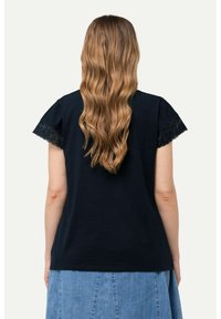 Camiseta de manga corta azul marino con puntilla en las mangas. La tela parece suave y tiene un corte holgado, combinada con una falda de mezclilla.