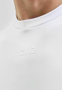 Vit t-shirt med kort ärm, tillverkad av mjukt tyg, med en liten upphöjd "CNZ"-logga på bröstet. Rund halsdesign.