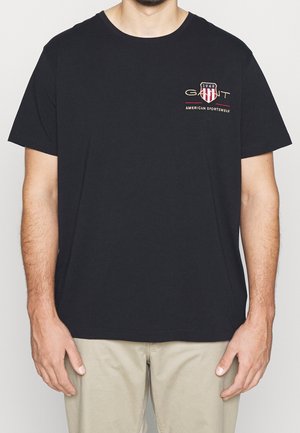 Czarna bawełniana koszulka z krótkimi rękawami, okrągłym dekoltem oraz małym wyhaftowanym logo w kolorze czerwonym i złotym na lewej stronie klatki piersiowej.