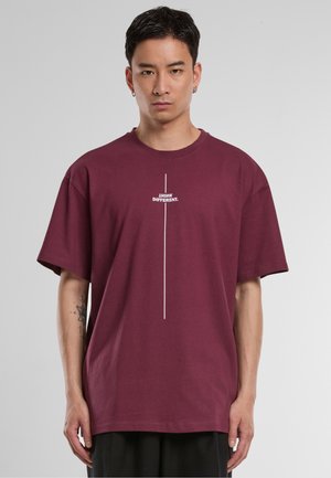 Burgunderfarget bomulls T-skjorte med korte ermer, med et horisontalt hvitt tekstgrafikk som leser "JEG TENKER FORSKJELLIG." Sentrert design.