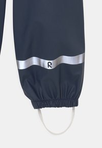 Námořnické voděodolné kombinézy se stříbrným reflexním pruhem a logem v dolní části. Obsahují elastické manžety a ramenní popruhy.