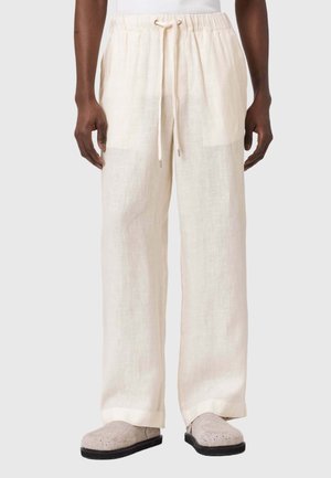 Lniane spodnie w jasnym kremowym kolorze z elastycznym pasem i sznurkiem do wiązania. Luźny krój i lekka tekstura. Noszone z szarymi klapkami.