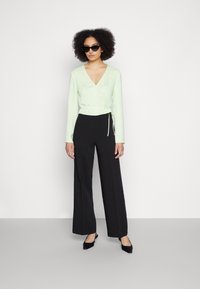 Top de manga longa verde menta com detalhe de laço, combinado com calças pretas de perna larga de cintura alta e sapatos de salto agudo pretos.