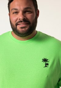 Osvětlené zelené bavlněné tričko s krátkým rukávem a kulatým výstřihem, které má na levé straně hrudi malou černou grafiku palmy.