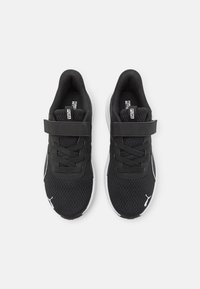 Chaussures de sport noires avec une tige en mesh, fermeture à lacets et bande velcro, semelle blanche et détail de logo sur le côté.