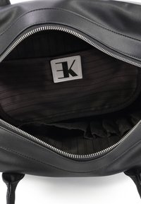 Zwart leren tas interieur met een horizontale ritssluiting, voorzien van een stoffen voering met een subtiel streepjespatroon en een merklabel.