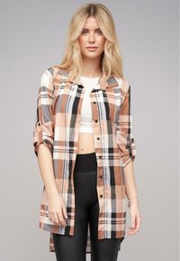 Rutet skjorte i fersken, sort og creme med opbrettede ærmer, parret med en hvid crop top og sorte leggings. Glat stoftekstur.