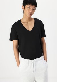 Sort V-udskåret T-shirt med korte ærmer, lavet af blødt stof. Sammen med lysegrå joggingbukser med elastisk talje og lommer.